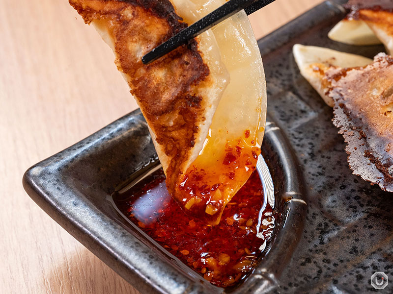 A close-up of Yaki Gyoza dipped into chili oil