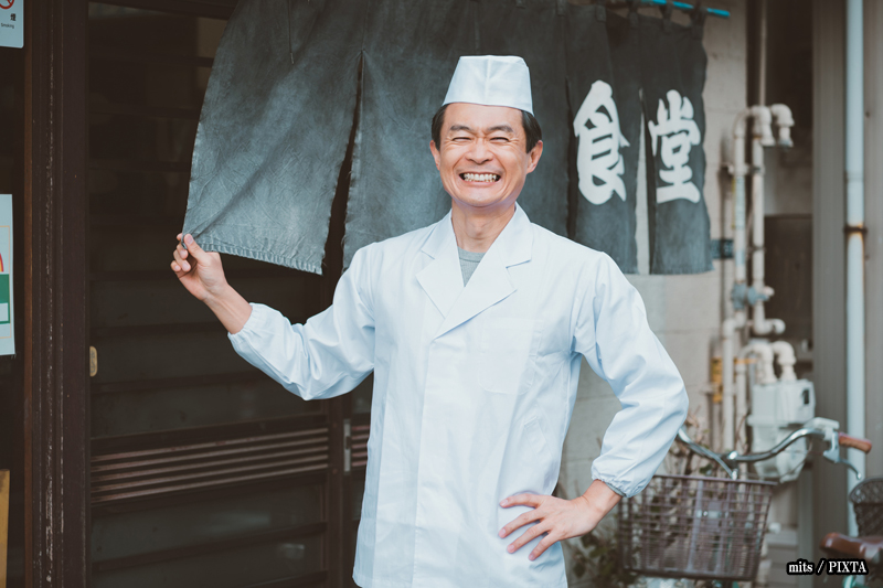 A Japanese shop owner standing in front of the noren curtain of his shop